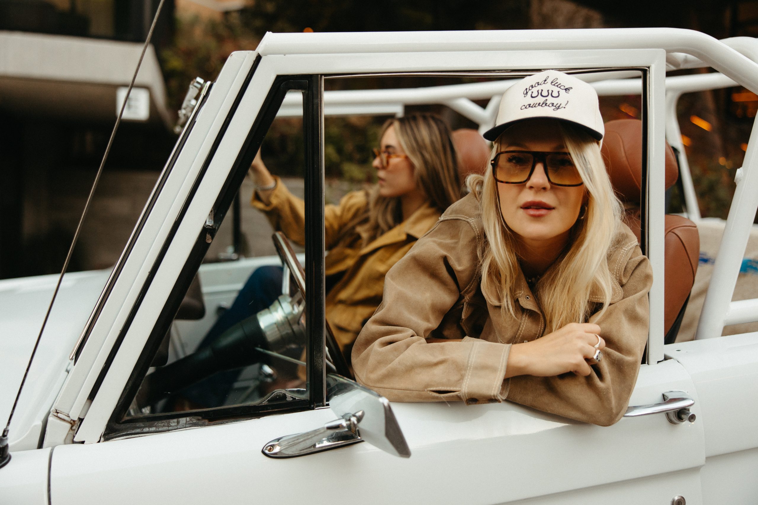 A woman with a hatr and sunglasses looks out through the open window of a rugged jeep.