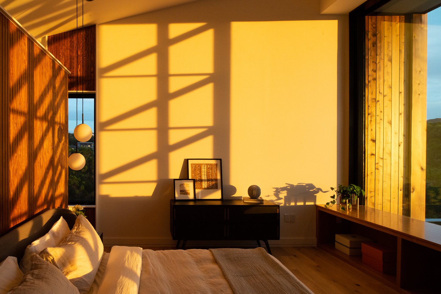 A large bedroom with a painting resting on a table, featuring a well-made bed, soft lighting, and minimal decor.