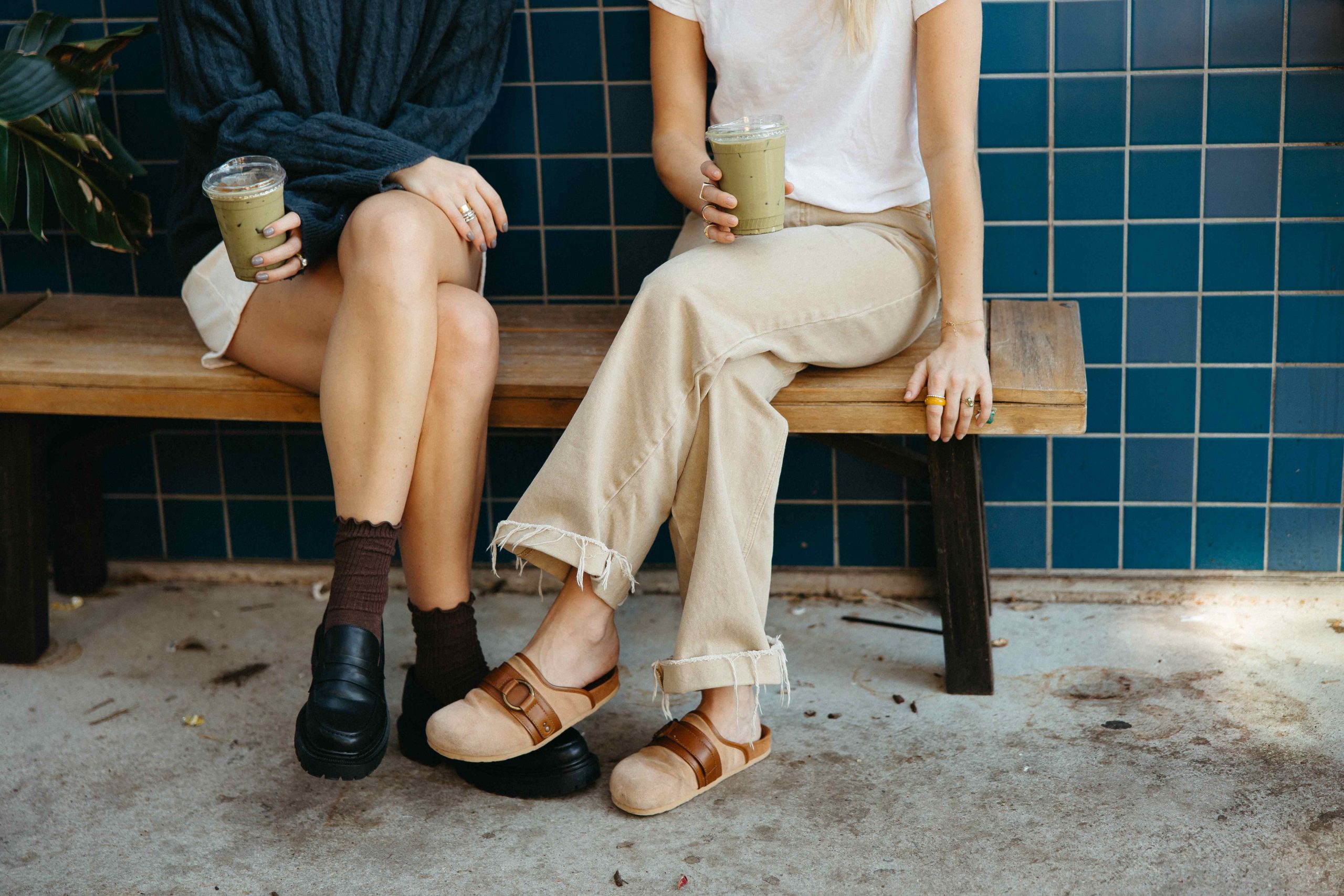 Two women sitting on a bench with a coffee in their hands