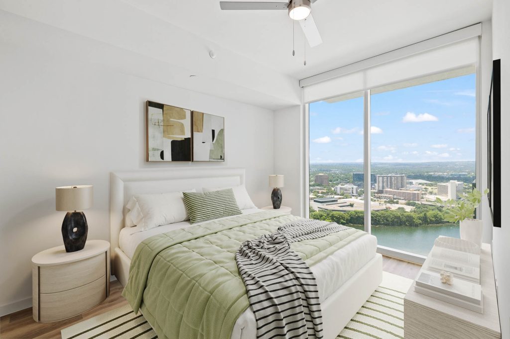 Bedroom with large windows overlooking Lady Bird Lake, featuring green bedding and minimalist décor.