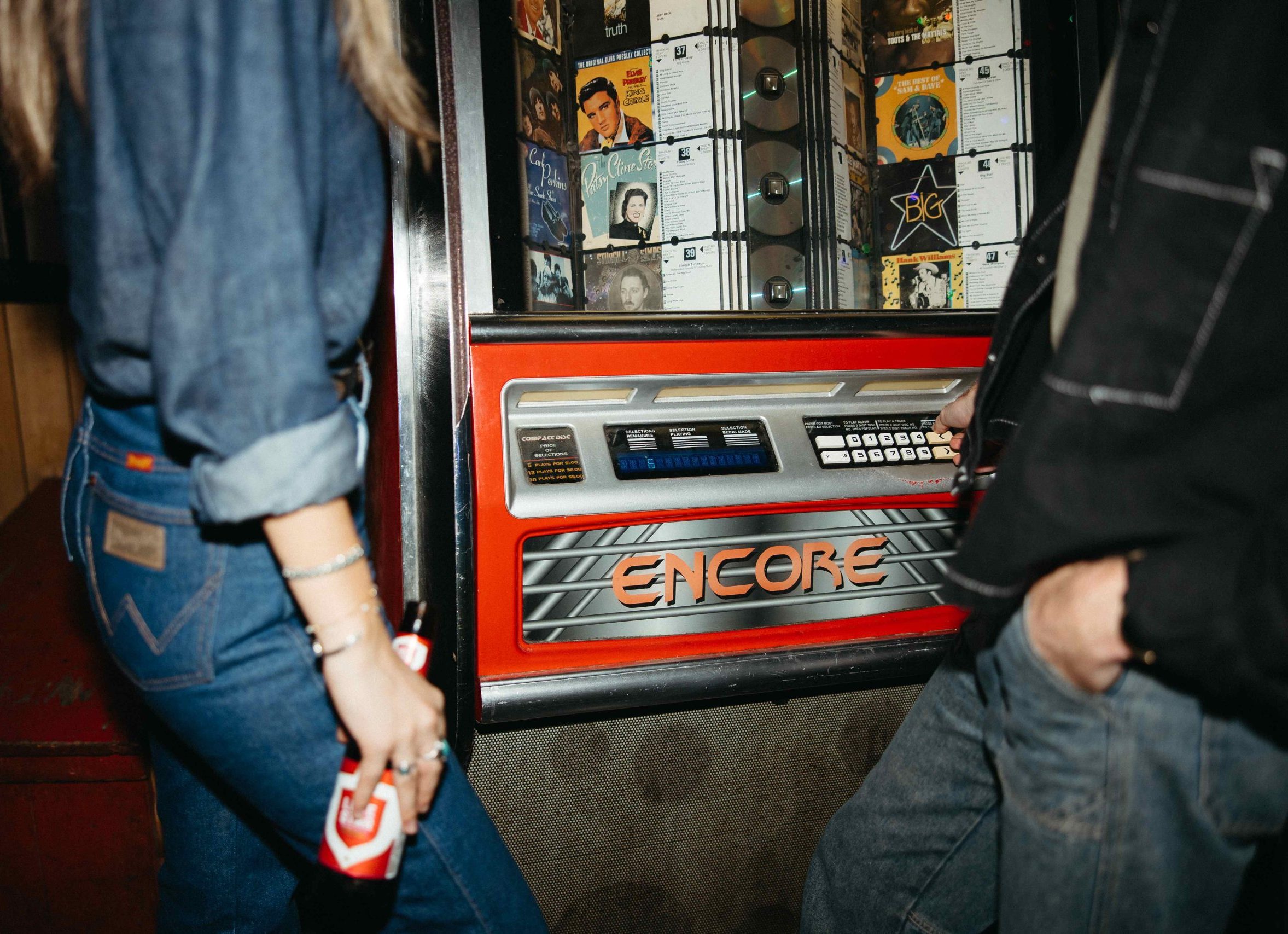 Two people standing in front of a red jukebox.