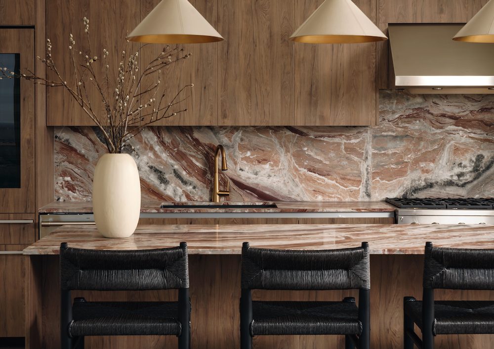 A modern kitchen with wood cabinets, a marble backsplash and countertop, matte black woven barstools, gold light fixtures, and a cream vase with branches on the island—perfect for luxury penthouses.