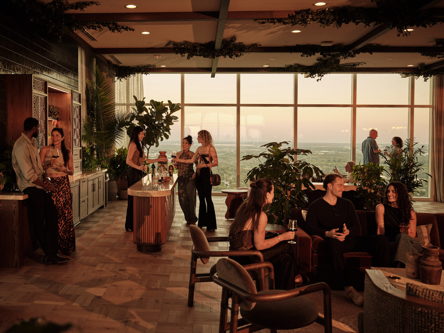 A group of people socialize in a stylish, modern lounge with large windows overlooking a scenic, sunlit landscape—just one of the inviting amenities at luxury apartments Austin TX residents love.