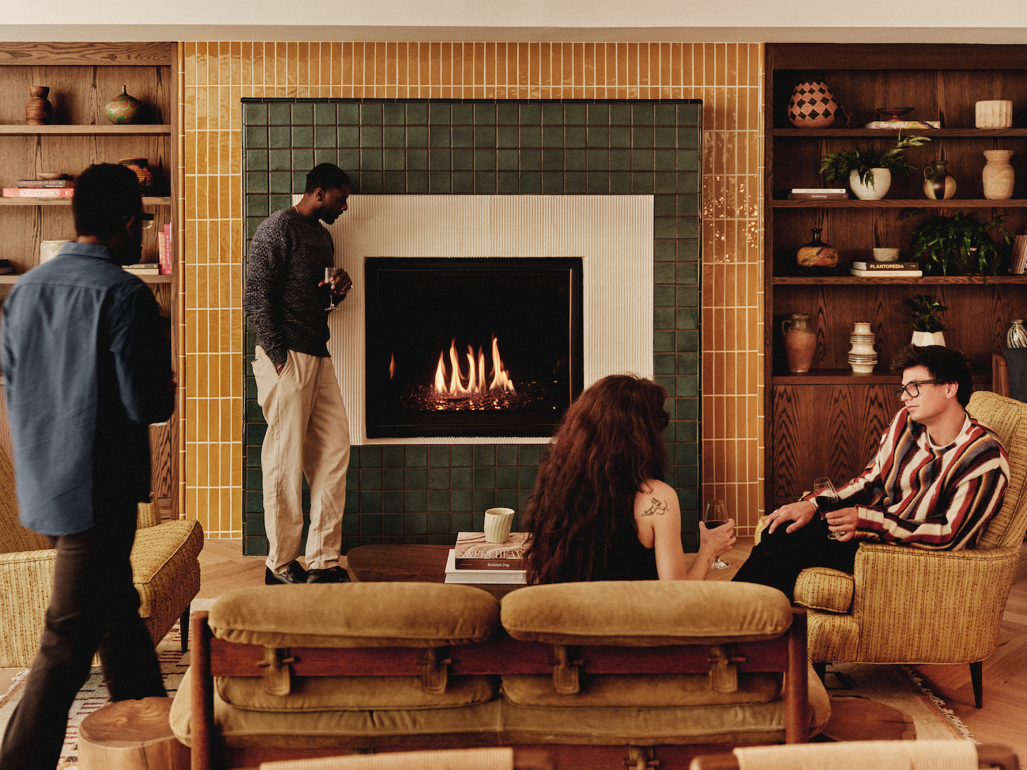 Four people relax in a cozy living room with a lit fireplace, enjoying drinks and conversation. Shelves with books and decor line the walls, capturing the inviting ambiance found in luxury apartments Austin TX offers.