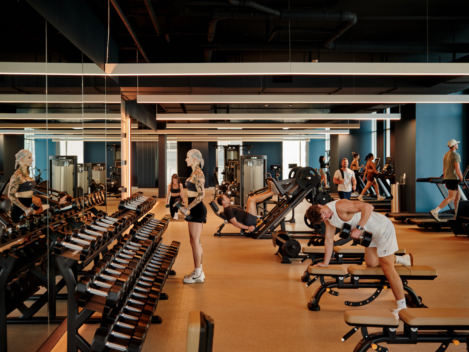 A modern gym within luxury apartments Austin TX, where people work out using dumbbells, benches, weight machines, and treadmills. The space features large mirrors and bright lighting for an energizing atmosphere.