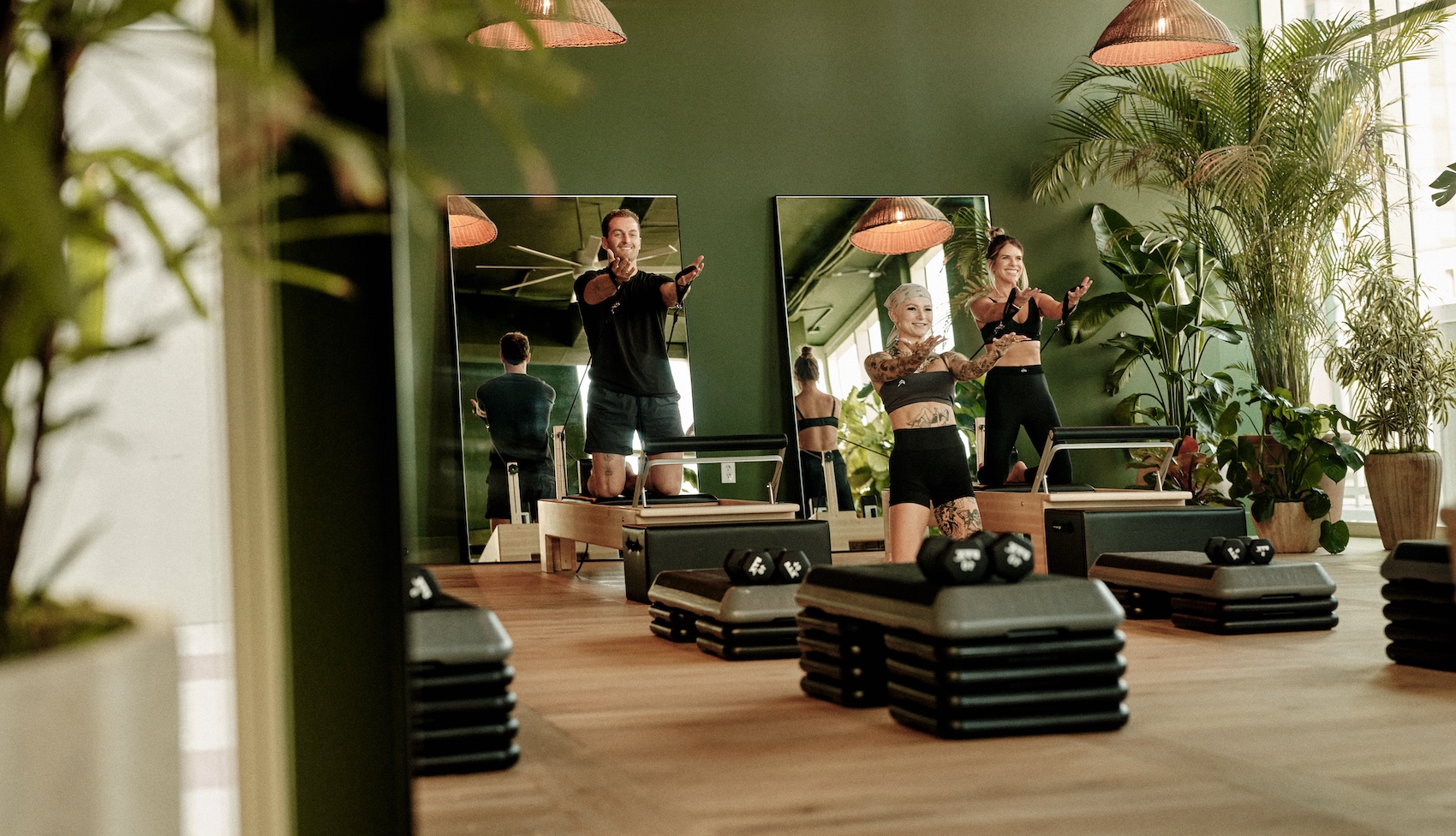 A group fitness class is exercising in a bright, green-walled studio with large mirrors, wooden floors, potted plants, and fitness equipment—just one of the top amenities offered by luxury apartments Austin TX residents enjoy.