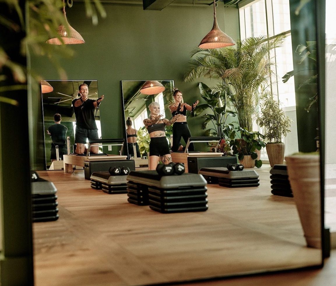 A group fitness class is exercising in a bright, green-walled studio with large mirrors, wooden floors, potted plants, and fitness equipment—just one of the top amenities offered by luxury apartments Austin TX residents enjoy.