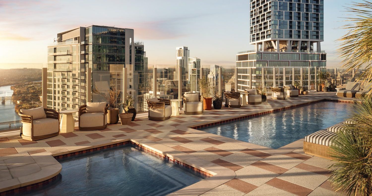 A rooftop pool surrounded by lounge chairs and potted plants overlooks a city skyline filled with modern buildings and elegant penthouses at sunset. The scene is calm and luxurious, with warm light reflecting on the water.