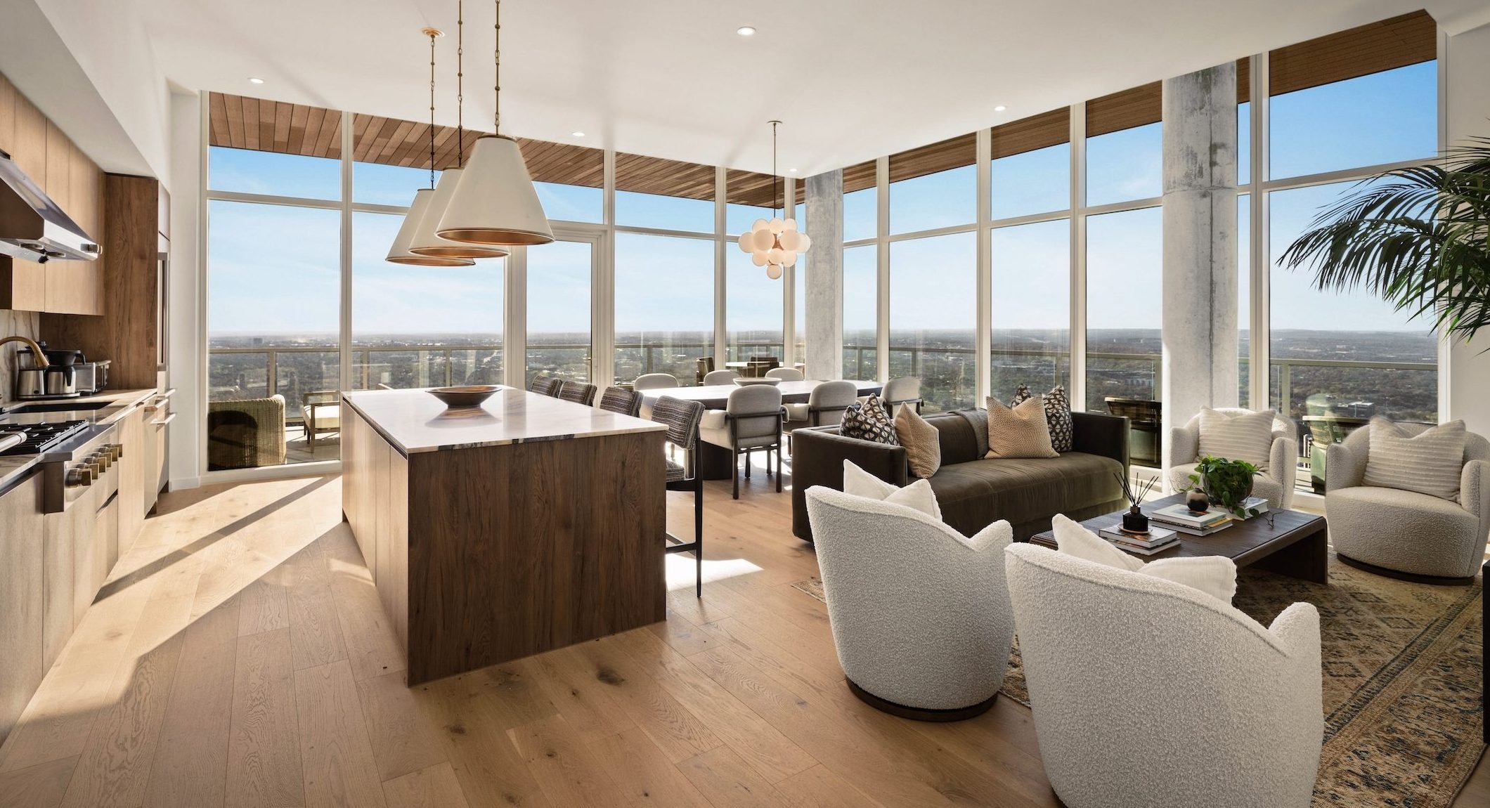 Modern open-concept kitchen and living room in the Paseo Penthouse, with floor-to-ceiling windows, wood floors, contemporary furniture, and city views; natural light fills the space, creating a bright and inviting atmosphere.