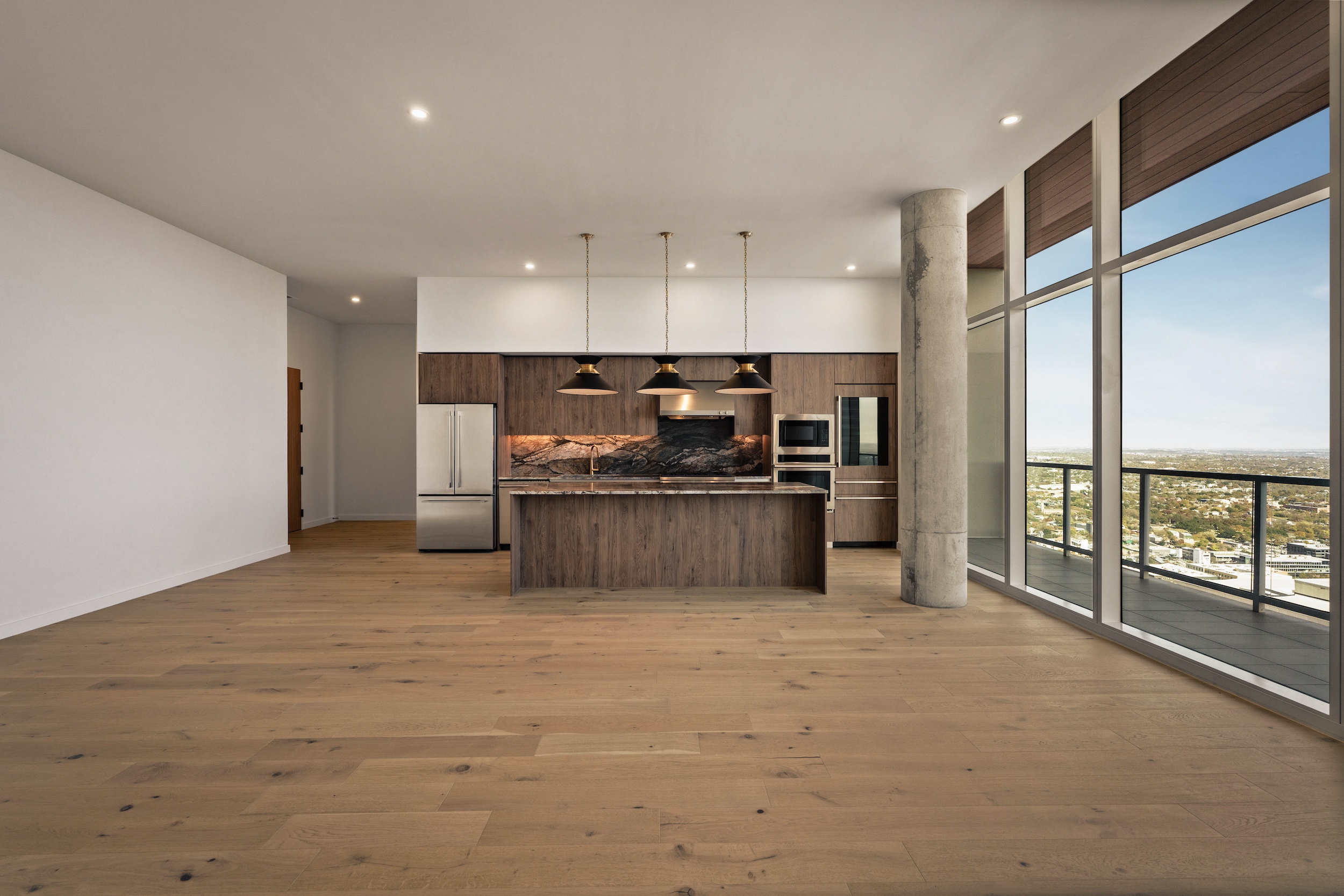 Modern open-concept paseo penthouse kitchen with wood floors, an island with pendant lights, stainless steel appliances, and floor-to-ceiling windows offering a city view.