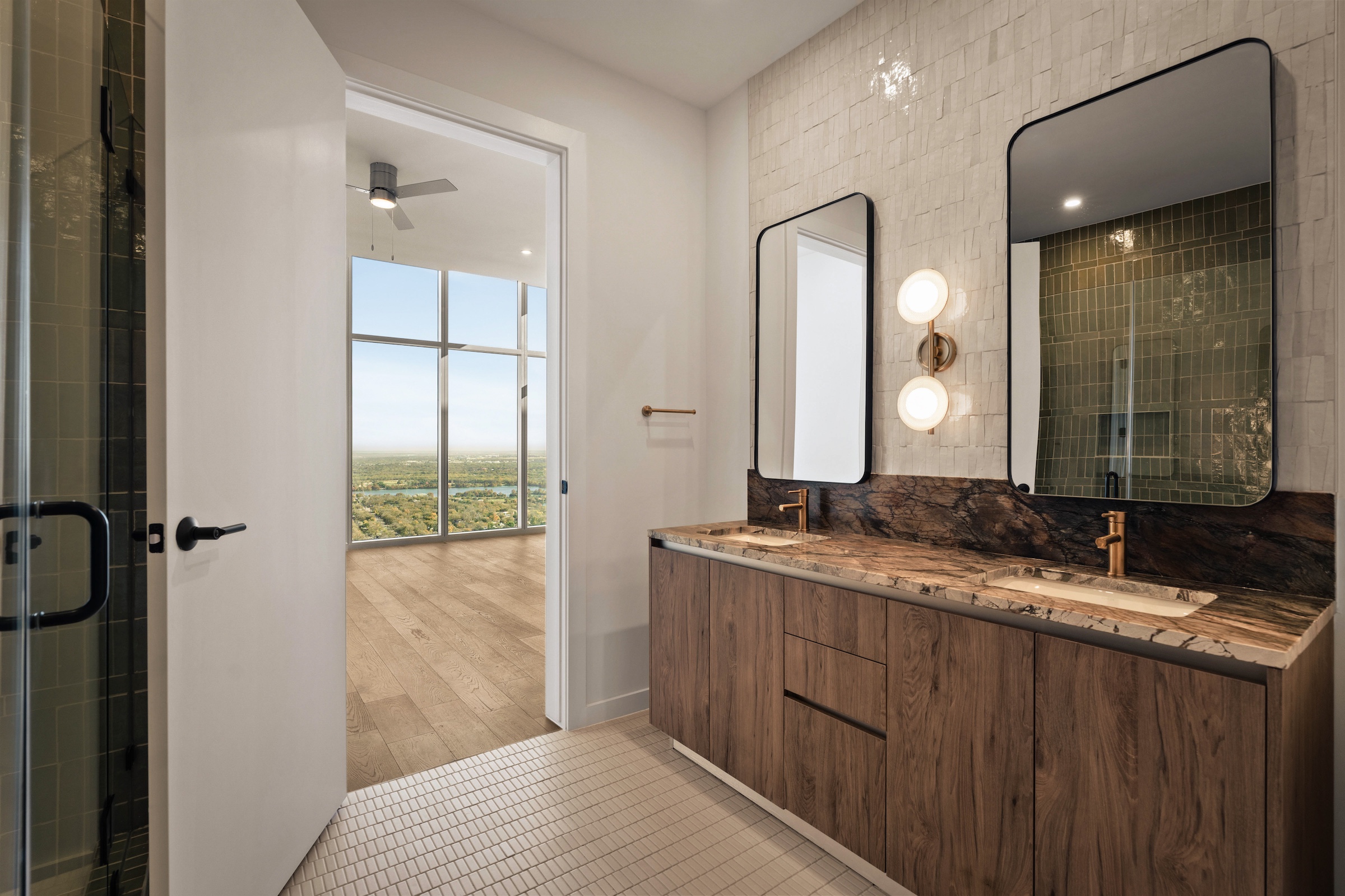 Modern bathroom in the Paseo Penthouse with double sinks, wooden cabinetry, two large mirrors, wall-mounted lights, and gold faucets. An open door reveals a bright room with floor-to-ceiling windows and a scenic outdoor view.