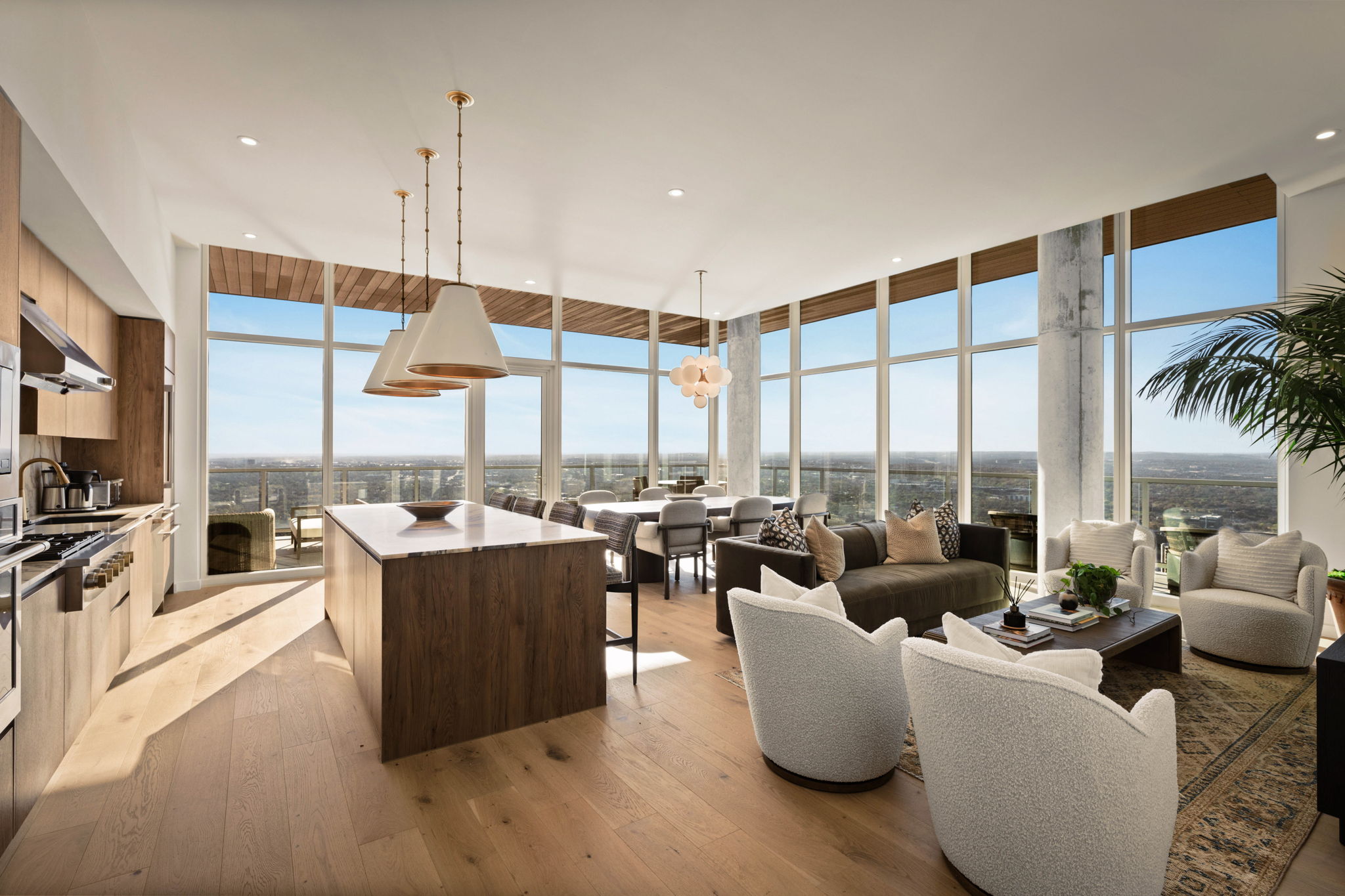 Modern paseo penthouse with floor-to-ceiling windows, wood floors, a kitchen island, dining area, and stylish living room furniture. Enjoy city skyline views and blue sky through expansive windows.