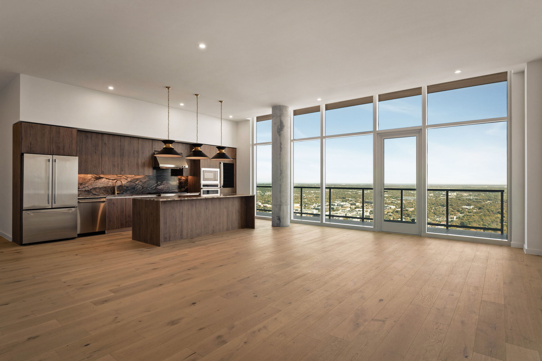 Modern, empty paseo penthouse with large windows offering a city view, an open kitchen with wooden cabinets, an island, pendant lights, built-in appliances, and light hardwood floors.